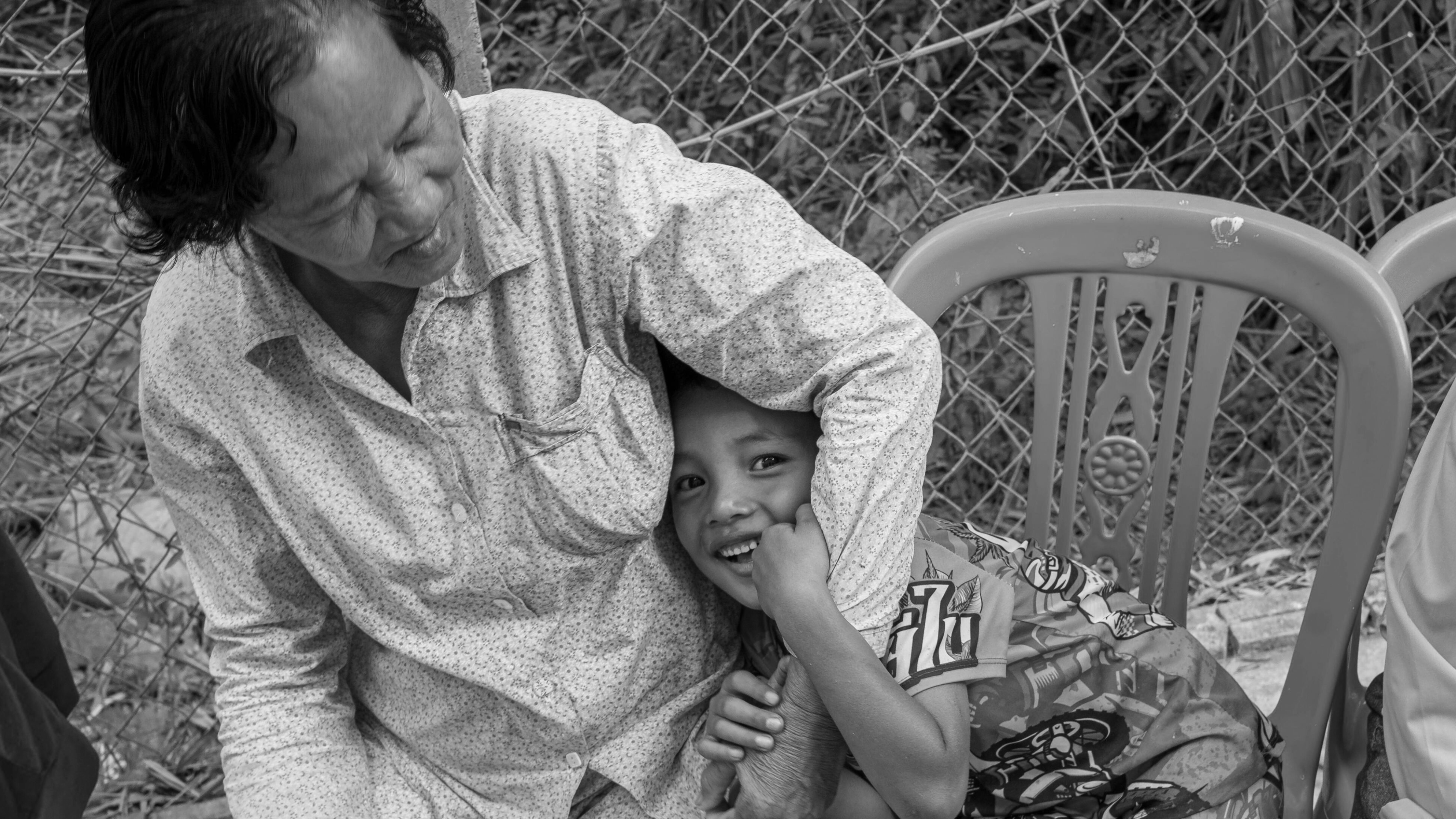 black and white photo of young boy hugging older woman's arms sitting in a chair